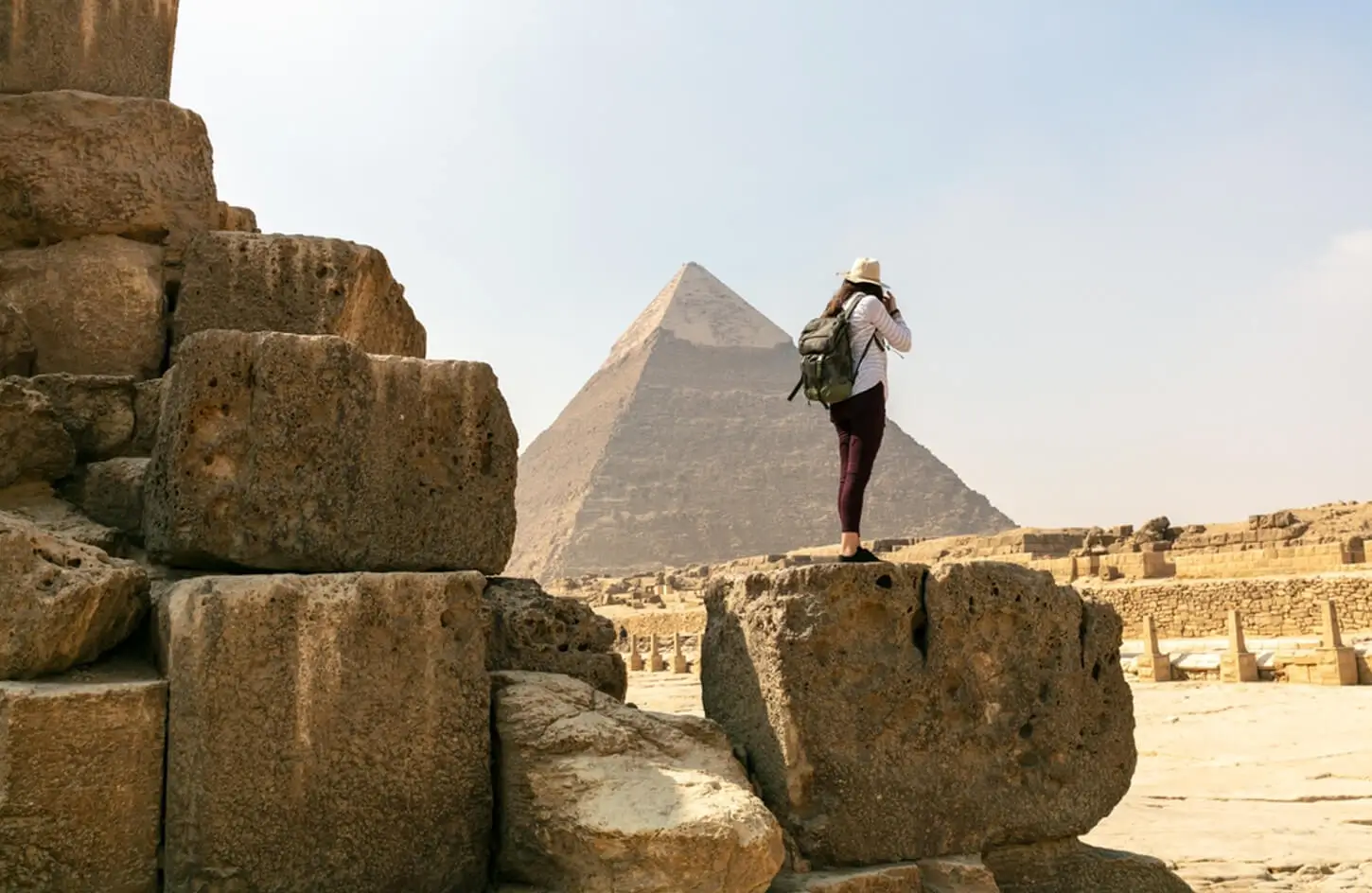 Tourist with a backpack standing on ancient ruins looking at the Giza Pyramids in Egypt.