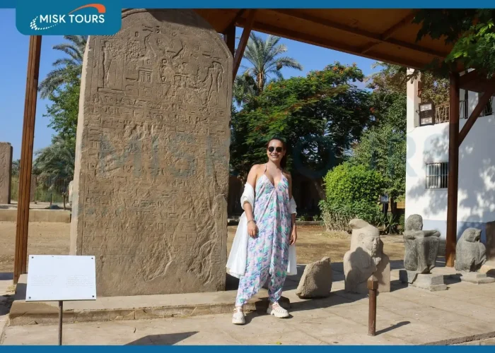 a-woman-in-a-patterned-jumpsuit-and-sunglasses-posing-by-an-ancient-hieroglyphic-stele-at-memphis-museum.