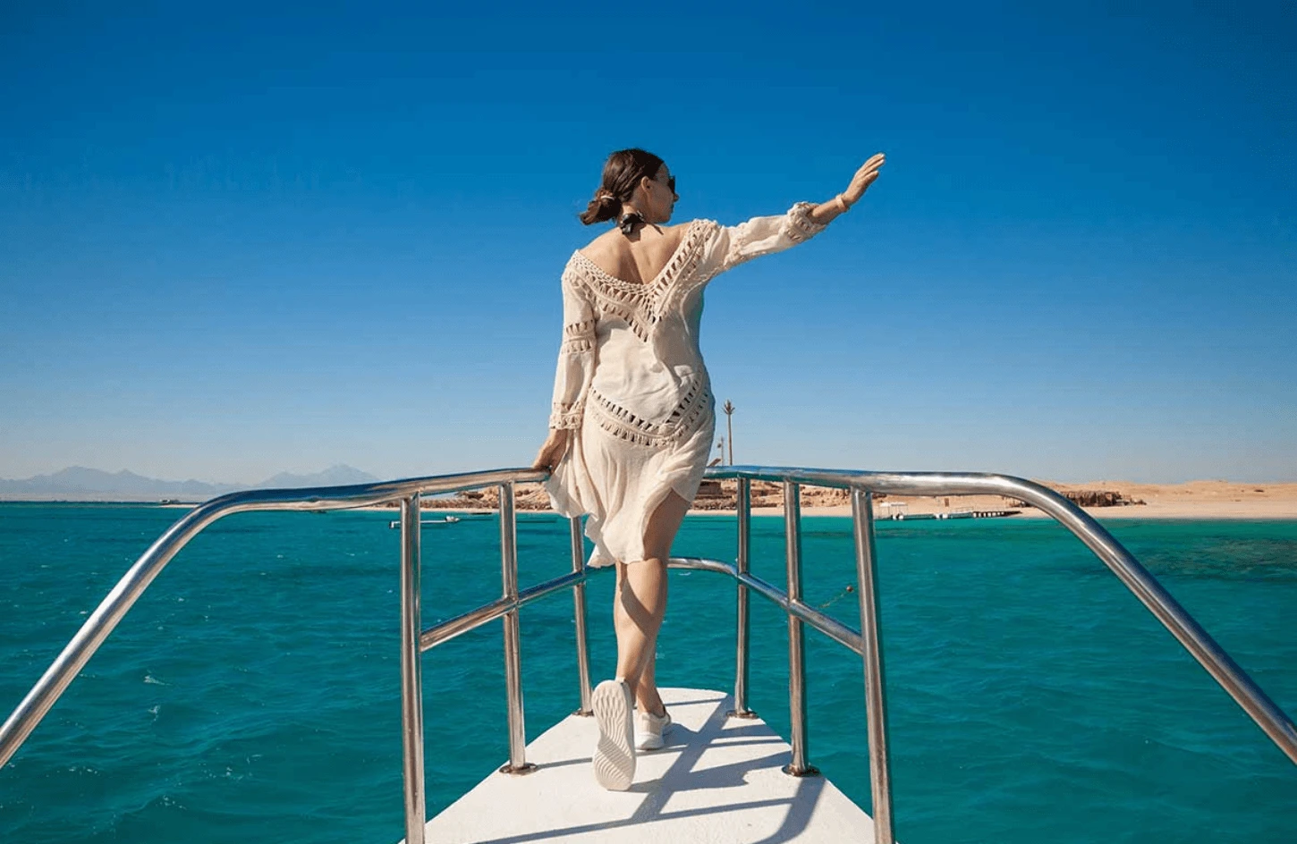 Woman in a white dress waving from the bow of a luxury boat during a Sharm El Sheikh boat tour on the turquoise waters of the Red Sea