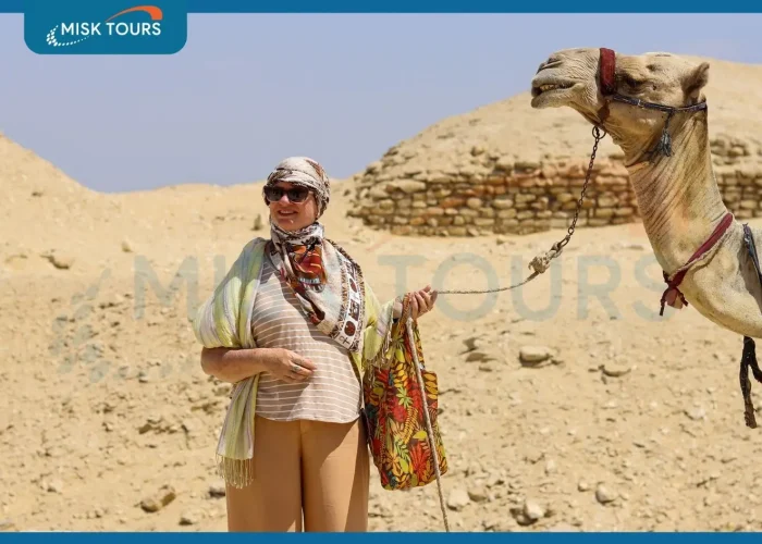 smiling-woman-tourist-holding-camel-reins-by-ancient-pyramid-ruins.