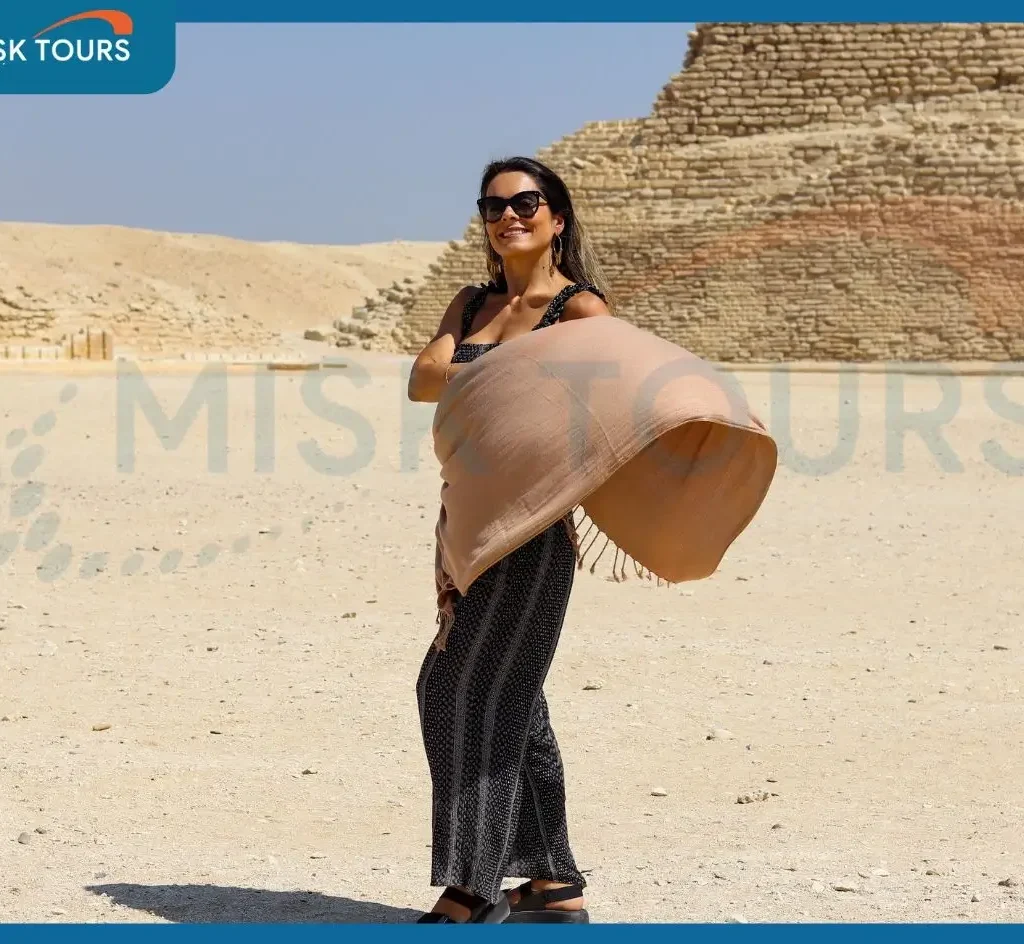 Smiling woman tourist holding flowing shawl at step pyramid of djoser saqqara.