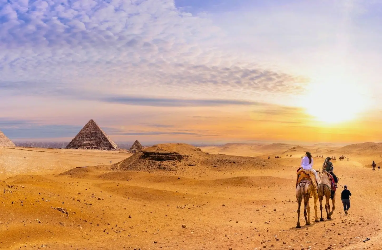 ourists riding camels through the desert at sunrise with the Giza Pyramids in the background, answering the question: How Many Days Do You Need in Egypt?
