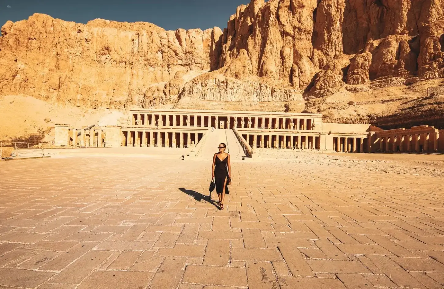 A woman in a black dress walking in the courtyard of the Mortuary Temple of Hatshepsut in Luxor, a highlight of a perfect 10 days in Egypt itinerary.