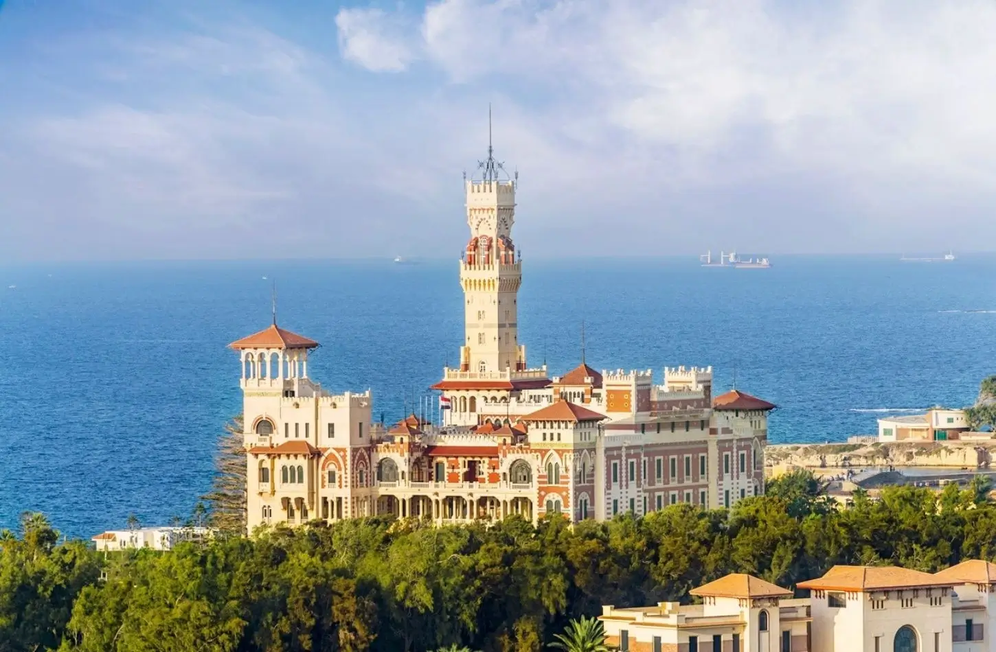 Historic Montaza Palace with its tall clock tower surrounded by green trees on the Mediterranean coast, highlighting popular things to do in Alexandria.
