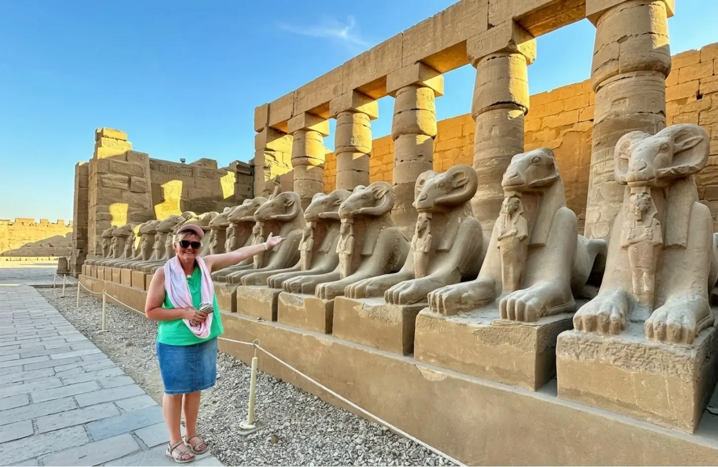 things-to-do-in-luxor-tourist-avenue-of-sphinxes-karnak-temple A happy tourist posing alongside the iconic ram-headed sphinx statues at Karnak Temple, one of the best things to do in Luxor.