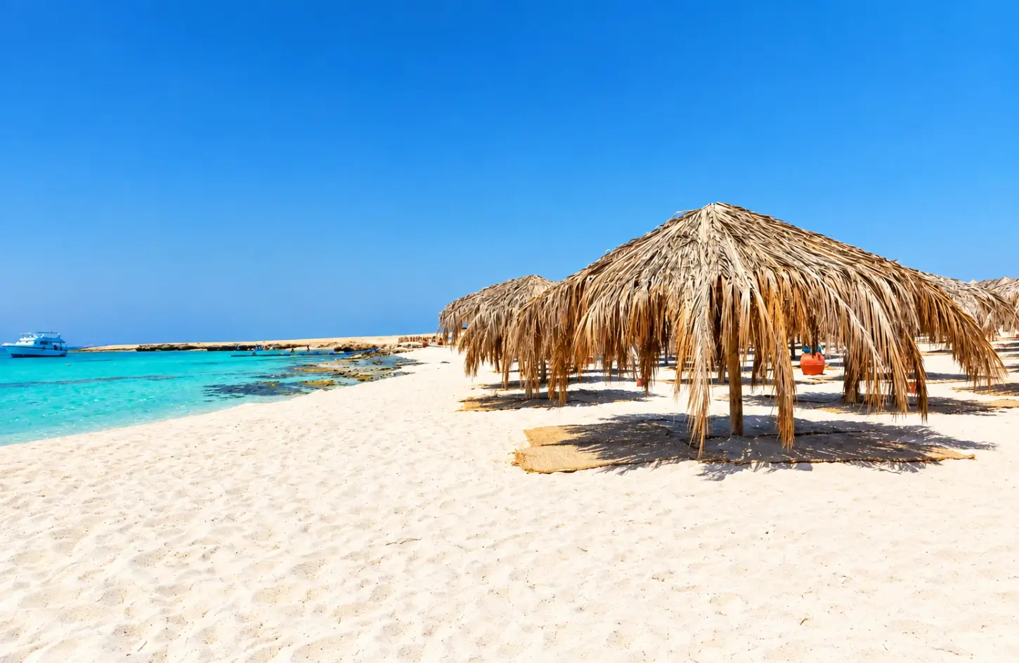 Relaxing on a white sand beach with straw umbrellas, one of the top things to do in Hurghada Egypt