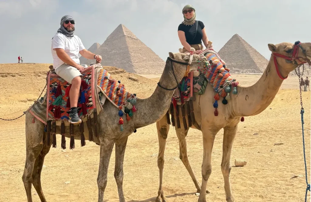 A stunning image of a man and a woman riding camels in the desert with the pyramids in the background